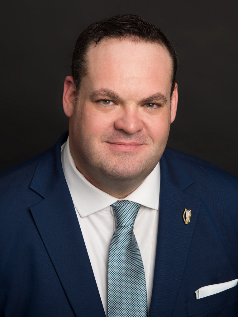 Professional headshot of a male finance executive on a gray background in Astoria, Queens