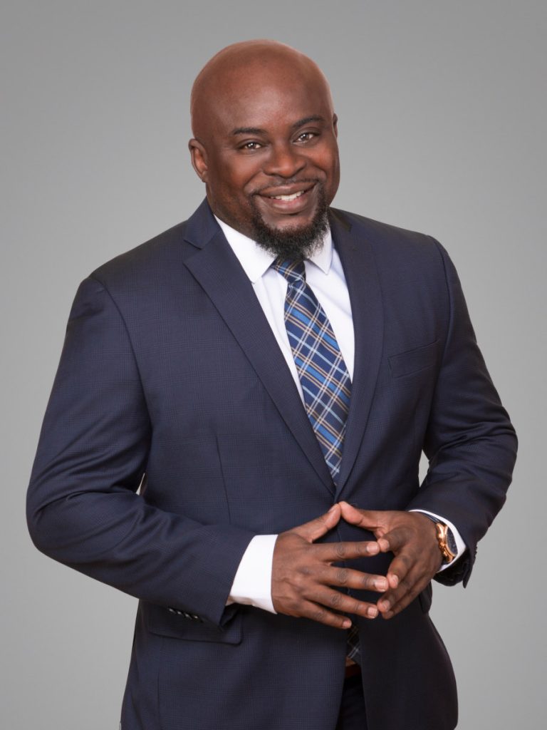 Professional headshot of a male financial advisor on a gray background in Downtown NYC